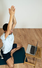 Caucasian Latino male performing a yoga session at home while following instructions from his...