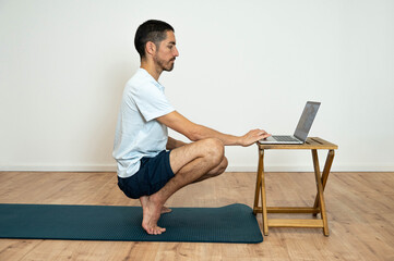 Fototapeta premium Yoga at home: Caucasian Latino man using his laptop for guided session