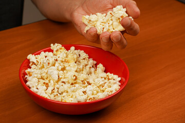 Salted popcorn. Popcorn .Fast food. Junk food. Snack for cinema. Flavored spicy popcorn scattered on table surface. Grabbing popcorn in hand. Delicious snack to eat in the cinema.