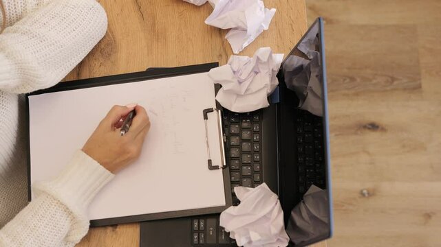 Woman working at her desk surrounded by crumpled paper. Crumpled paper scattered everywhere shows struggle with ideas, emphasizing effort. Perfect for themes of work stress and crumpled paper moments.