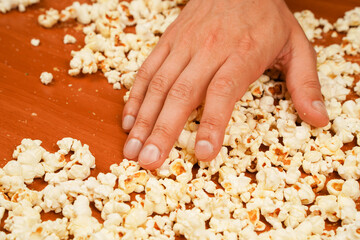 Flavored spicy popcorn in man's hands. Salted popcorn. Popcorn. Fast food. Junk food. Snack for cinema. Popcorn scattered on table surface. Delicious snack to eat in the cinema.
