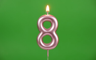Burning pink birthday candle on green background, number 8