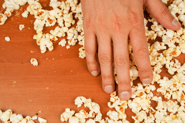 Popcorn scattered on table surface. Delicious snack to eat in the cinema. Flavored spicy popcorn in man's hands. Salted popcorn. Popcorn. Fast food. Junk food. Snack for cinema.