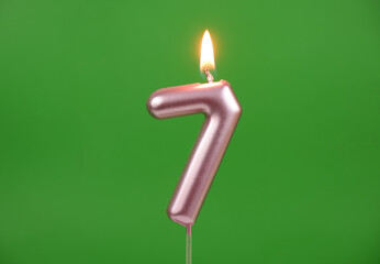 Burning pink birthday candle on green background, number 7