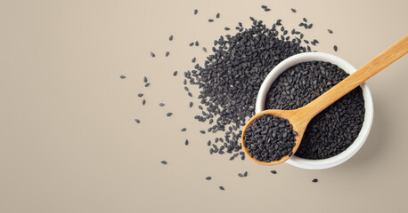 Black sesame seeds wood spoon on white bowl with on brown background, top view