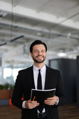 A man in a suit holding a book and a pencil. He is smiling and he is happy