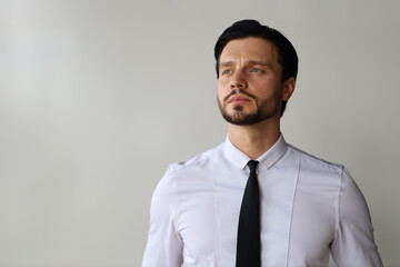 A man wearing a white shirt and black tie is looking at the camera. He is deep in thought