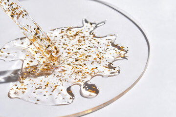 Liquid gel serum with gold particles spreading on transparent surface in minimalist beauty and skincare concept