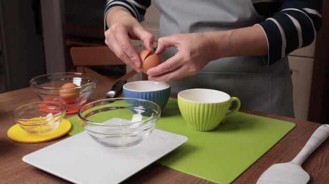 Process of making dough. Woman separates egg white from yolk in kitchen. Scales and eggs, utensils on wooden table. Baking macarons at home. Hands in close-up.