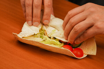 Fast food. Junk food. Eating. Food. Delicious. Preparing chicken roll. Tortilla wrap with fried chicken meat and vegetables, close up. Shawarma tomato, cucumber, onion, lettuce and chicken meat.