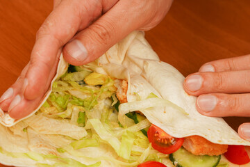 Cooking chicken roll. Tortilla wrap with fried chicken meat and vegetables, close up. Shawarma tomato, cucumber, onion, lettuce and chicken meat. Fast food. Junk food. Eating. Food. Delicious.