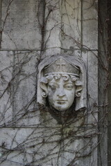 The carved stone face of a Christian woman peeking thru the stone wall.
