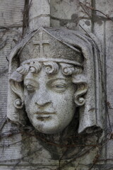 The carved stone face of a Christian woman peeking thru the stone wall.