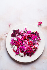 Edible pink culinary flowers on white plate, on pink marble background.