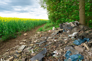 Litter strewn across rural path next to vibrant yellow fields under cloudy sky on overcast day