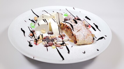 Plated dessert with ice cream and fruit strudel. A beautifully plated dessert consisting of a slice of fruit strudel and scoops of ice cream, garnished with assorted nuts and drizzled with chocolate