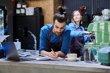 Two cafe workers working together behind counter, at coffee shop