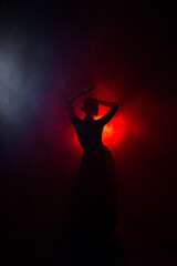 Silhouette of a woman in a red skirt dancing Latin in smoke in neon light. Dance concept. Bachata,...