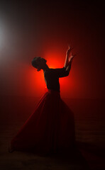 Silhouette of a woman in a red skirt dancing Latin in smoke in neon light. Dance concept. Bachata,...