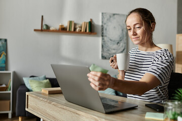 A beautiful woman with vitiligo sips coffee while engaging with her laptop.