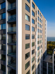 A drone flyby showcasing a modern high-rise building with sleek balconies and large windows. The ocean and surrounding greenery in the background enhance the urban-coastal appeal