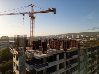 A drone video capturing the construction site of a high-rise building at sunset. The structure's concrete framework, cranes, and scaffolding are bathed in warm sunlight, highlighting urban development