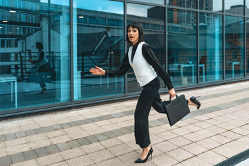 Young businesswoman hurrying with a briefcase along a modern office building during a busy workday