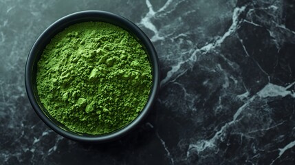 Matcha green tea powder displayed in a black ceramic bowl on a white marble table, emphasizing vibrant green color and fine texture under moody lighting in an overhead food photography view.