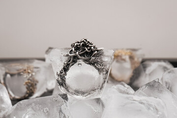 Close-up and macro shots of silver jewelry on a background of ice cubes. Silver ring in ice cube isolated on white background. Metal decoration in an ice cube.