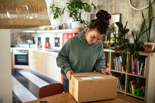 Young woman opening cardboard box package at home