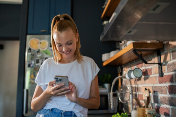 Smiling young woman using smartphone in modern kitchen