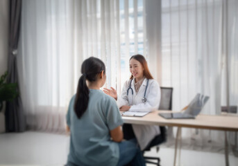 Obraz premium A woman in a white lab coat and stethoscope is sitting at a desk talking to another woman in a blue shirt.