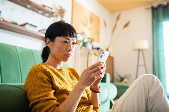Serious woman looking at phone while sitting on couch