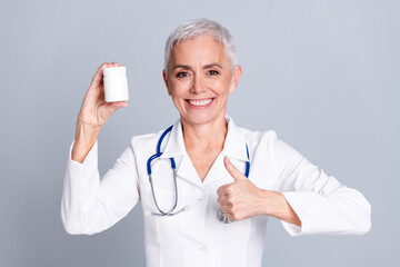 Portrait of aged woman professional doctor thumb up pills wear white coat isolated on grey color background