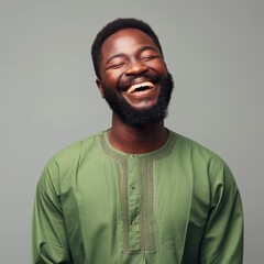 Obraz premium A cheerful Nigerian man in his 40s with short black hair, wearing a green traditional attire, smiling broadly against a neutral background.