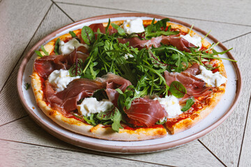 Pizza with prosciutto, arugula and cheese in wooden desk