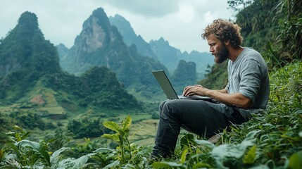 A man works on his laptop in a serene mountain landscape, blending technology and nature seamlessly.