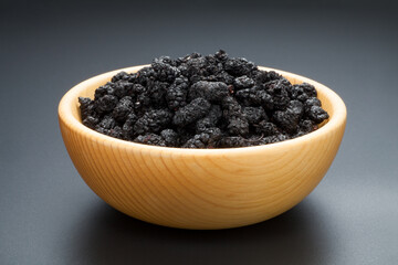 Dried black mulberries in a wooden bowl on black background