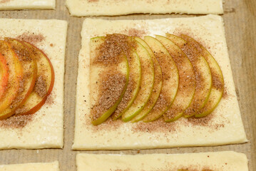 Sliced apples on pastry with sugar and cinnamon for baking preparation.