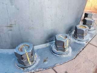 Close-up of large industrial bolts with yellow alignment markings. The bolts are attached to a gray...