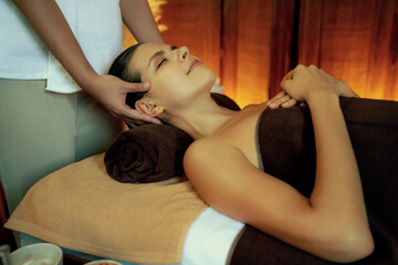 Caucasian woman enjoying relaxing anti-stress head massage and pampering facial beauty skin recreation leisure in warm candle lighting ambient salon spa in luxury resort or hotel. Quiescent