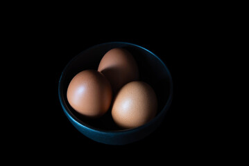 Chicken eggs in a black bowl on black background
