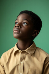 Fototapeta premium Reflective teenager Black boy in a semi-formal shirt, with a contemplative expression on a green studio background.