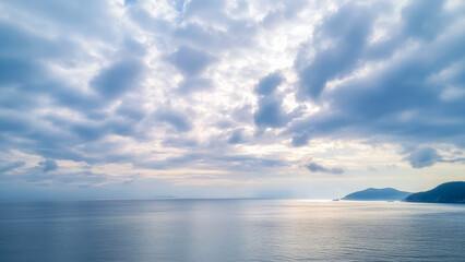 Obraz premium Calm ocean waters and dramatic clouds create a serene atmosphere at sunset along the coast