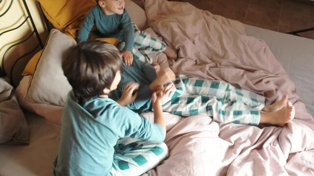 Two children tickling their brother lying on a bed.