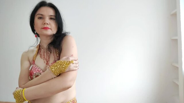 A dancer in a red suit is dancing an oriental dance on a white background. A professional dancer dances oriental belly dance. Sexy woman in red dress dances a seductive dance in a white studio