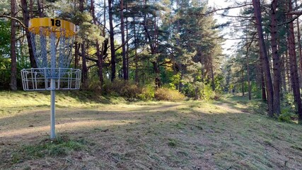 Disc golf basket number 18 in Ventspils park, Latvia, surrounded by autumn trees during October 2024, under a clear sky, ideal for outdoor sports, recreation, and active lifestyle – static shot