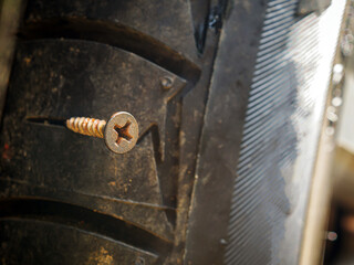 Close-up of a rusty screw driving into a car tire causing a puncture.
