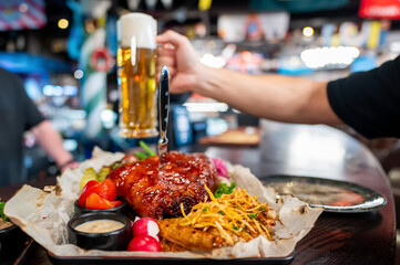 A close-up of a pub meal featuring a glass of beer, grilled chicken, fries, and salad on a wooden table. The warm lighting and rustic setting create a cozy dining atmosphere.