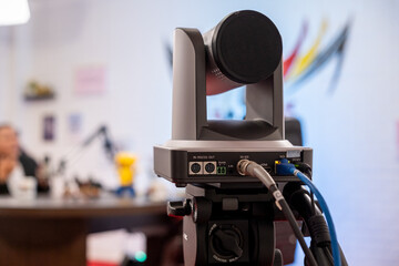 PTZ camera connected with HDMI, 3G-SDI, NDI, and DC12V cables, capturing a livestreaming podcast video in a content creator studio with a blurred background for depth.
